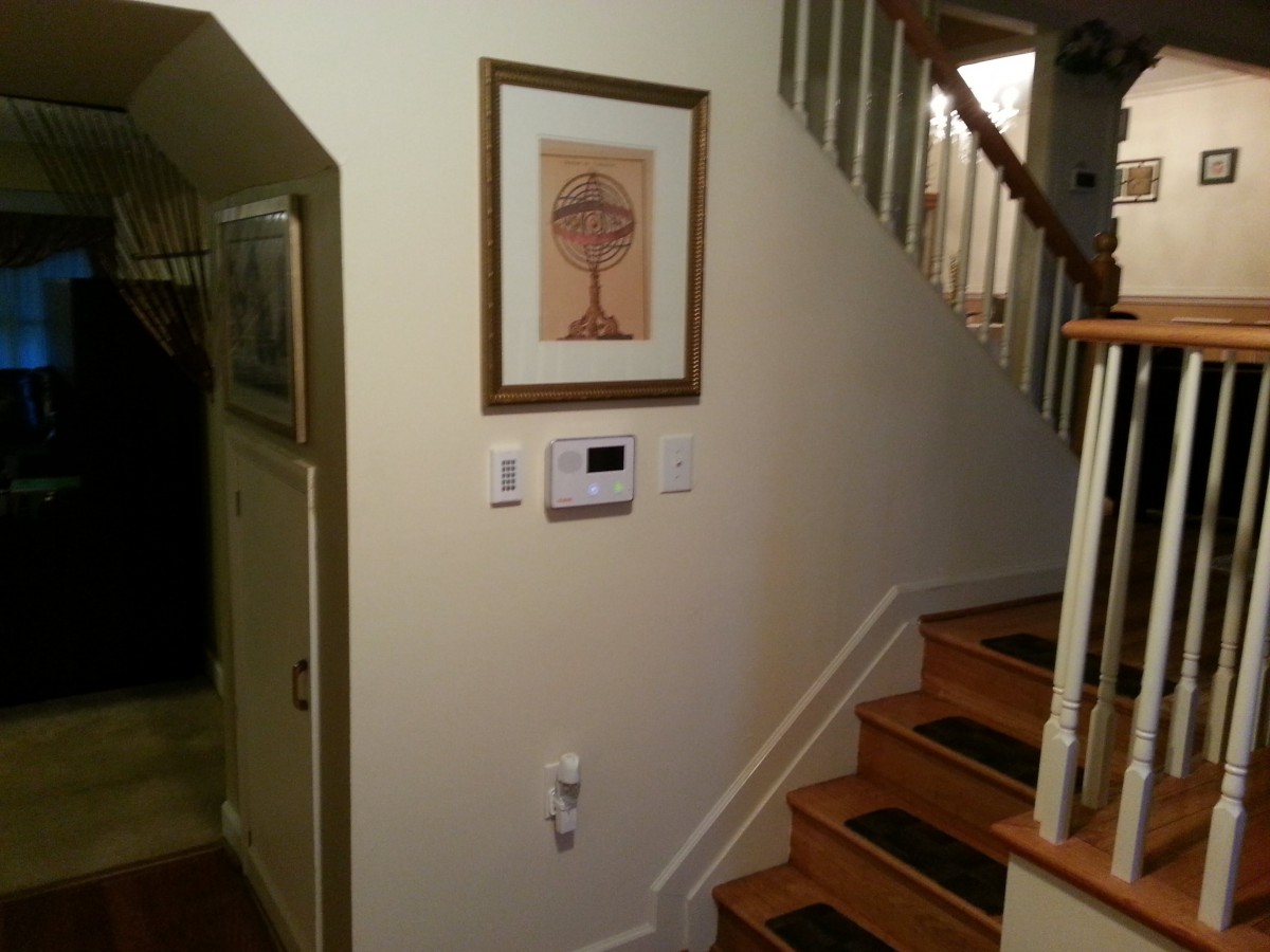 A view of a staircase in a hallway with a picture frame and thermostat on the wall.