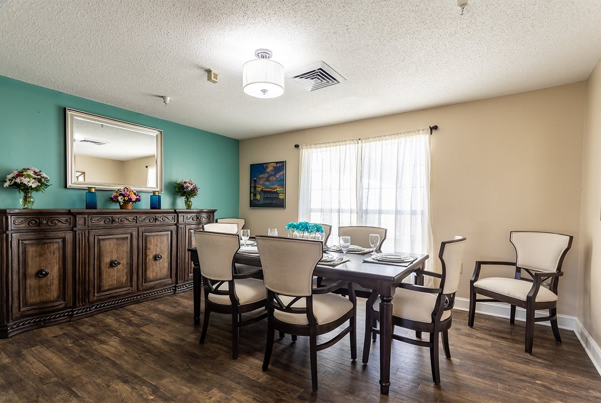 A well-lit dining area with a wooden table and chairs, featuring artwork and decorative elements.