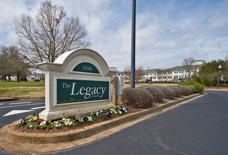 Entrance sign for The Legacy Apartments with surrounding landscaping.