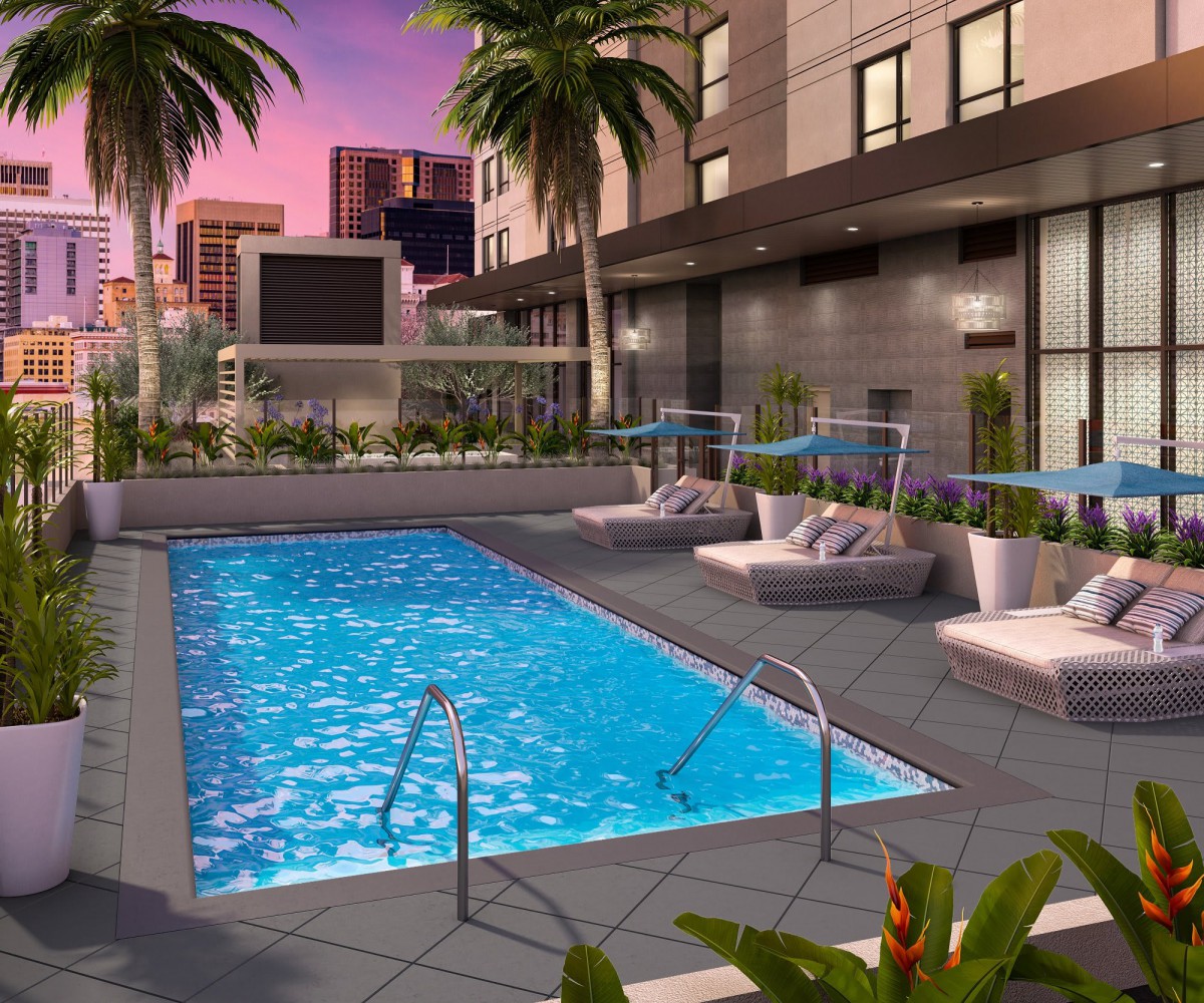 A luxurious outdoor pool area surrounded by palm trees with a vibrant city backdrop at sunset.