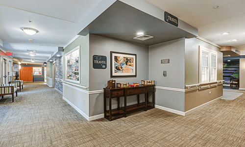 A well-decorated hallway with artwork and a wooden table, featuring carpeted flooring and recessed lighting.