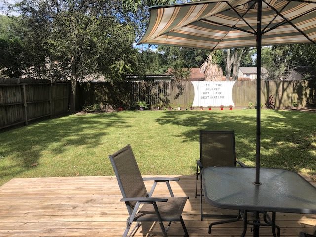 A sunny backyard with a wooden deck and patio furniture under an umbrella.