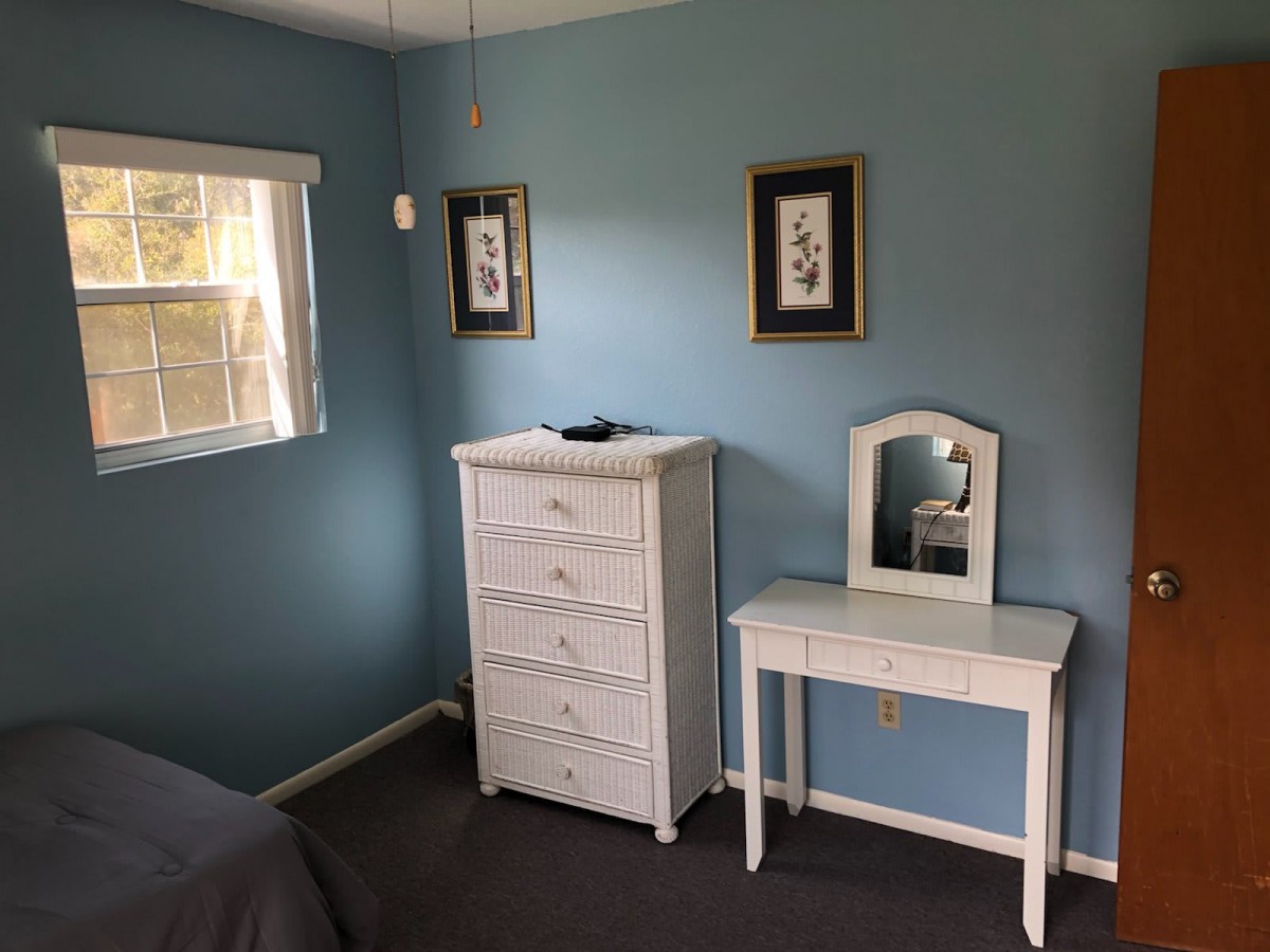 A cozy bedroom with blue walls, featuring a white dresser and vanity table, complemented by framed wall art.