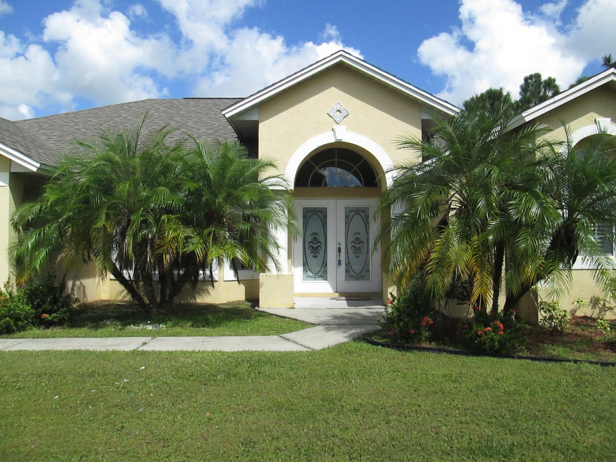 A suburban house with palm trees and a well-manicured front yard on a sunny day.