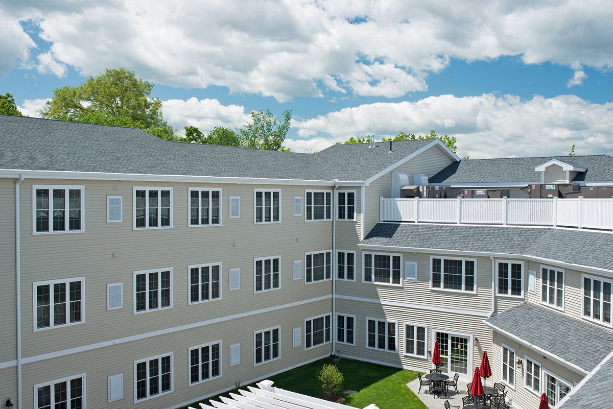 A multi-story residential building under a partly cloudy sky with greenery in the background.