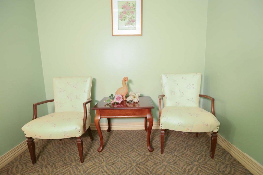 A waiting area featuring two chairs and a small table with a decorative ornament and flower arrangement.