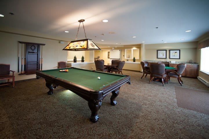 A spacious and elegantly designed game room featuring a pool table under a stylish light fixture.
