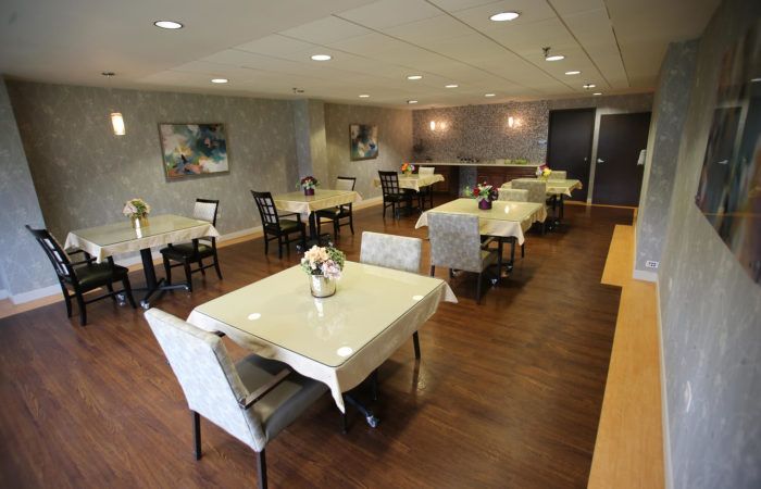 An elegant dining room with several neatly arranged tables and chairs, adorned with simple decor and soft lighting.