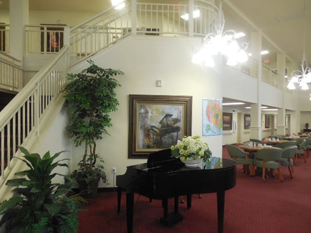 A cozy lobby with a grand piano, elegant staircase, and artwork on the walls.