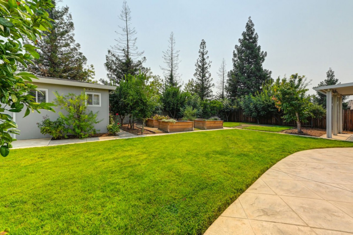 A well-maintained backyard with a lush green lawn, surrounded by trees and garden planters.