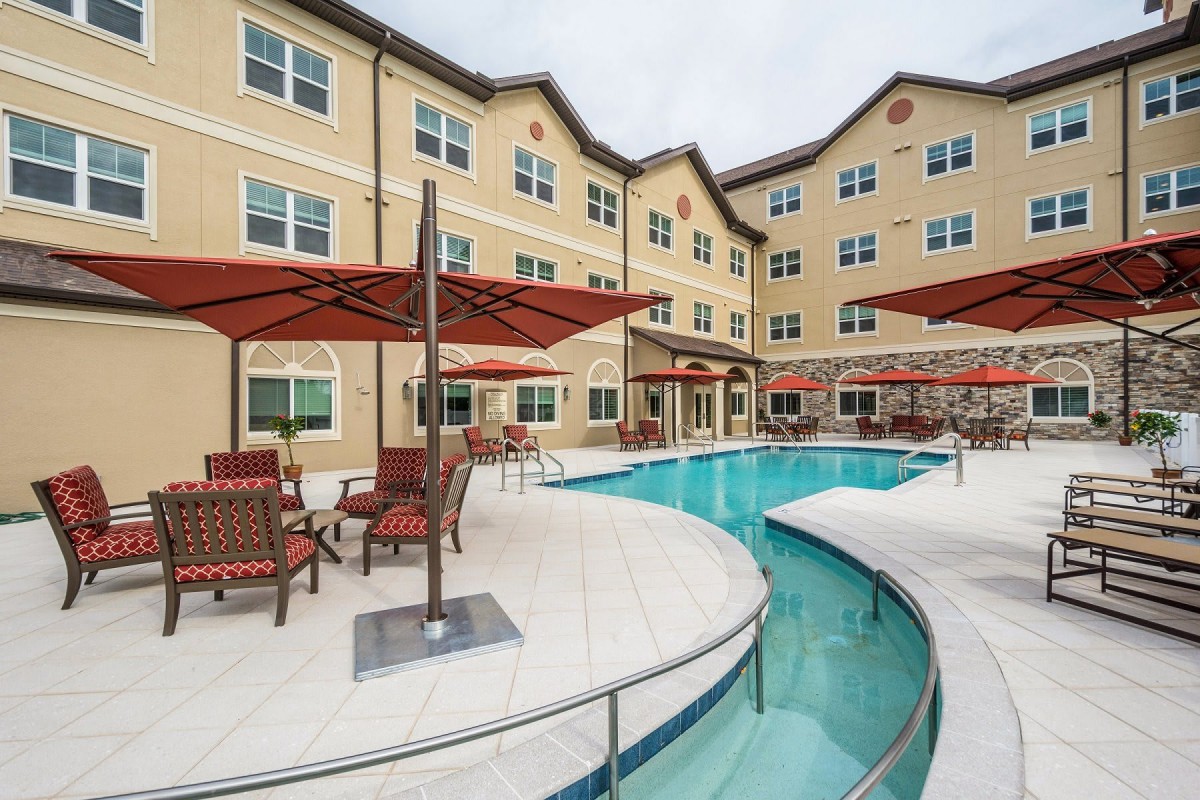 A hotel with a swimming pool and outdoor seating under umbrellas.