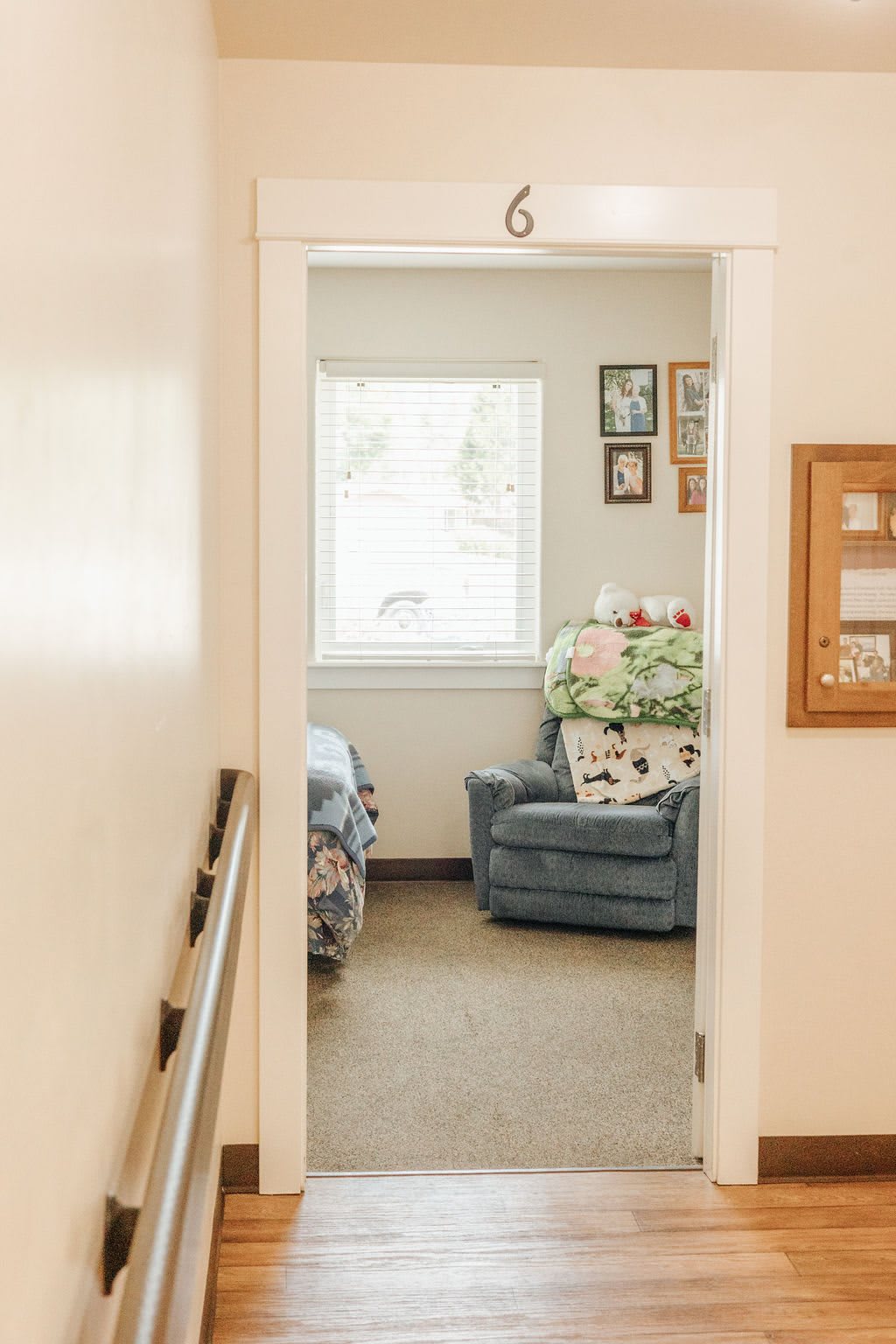 A cozy bedroom with a comfortable armchair, adorned with decorative pillows and wall art, viewed from a hallway.