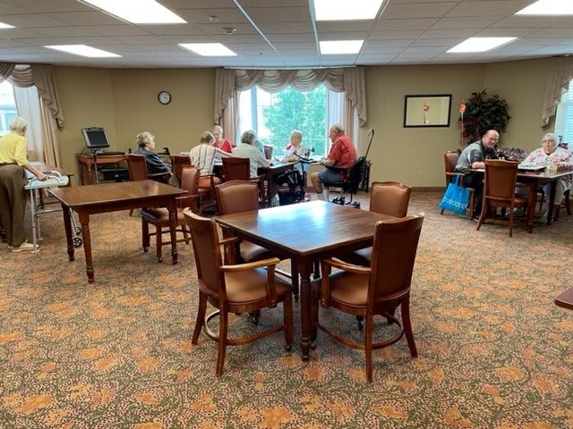 A group of seniors gathered in a community center, sitting at tables and engaging in conversation.