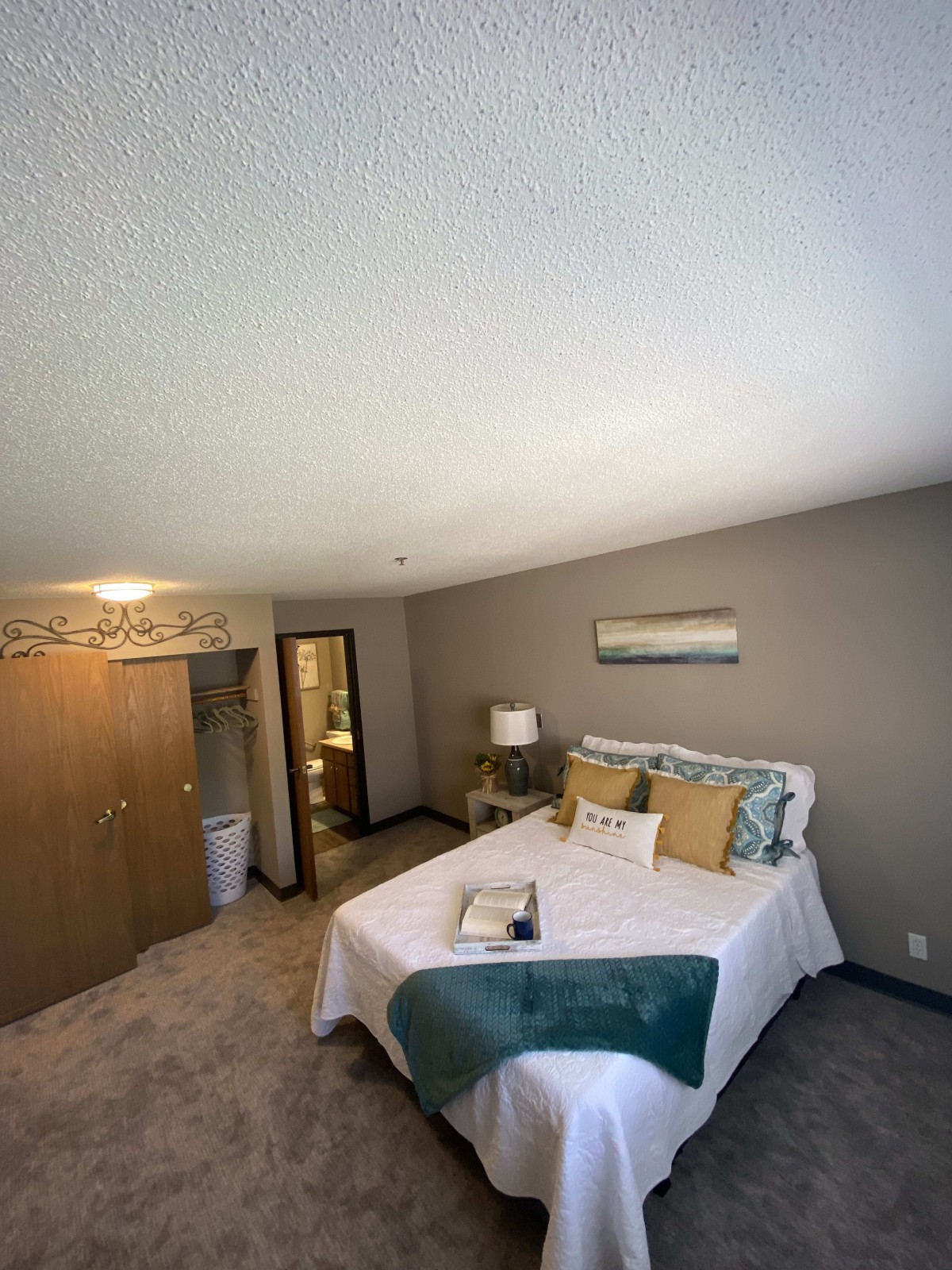 A well-decorated bedroom with a neatly made bed, warm lighting, and minimalist decor.