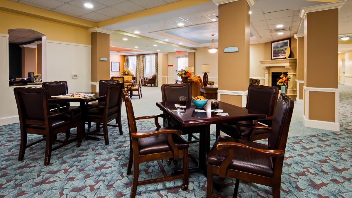 A well-decorated dining area with tables and chairs, featuring warm lighting and a carpeted floor.
