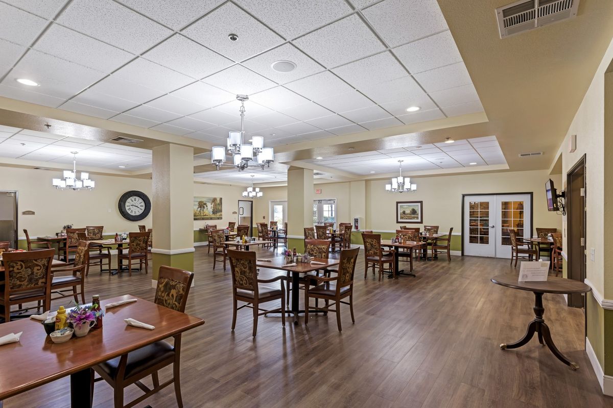An empty dining room with neatly arranged tables and chairs, featuring chandeliers and wooden flooring.
