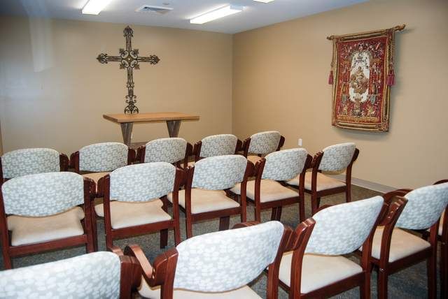 A small chapel with neatly arranged chairs facing a cross on the wall.