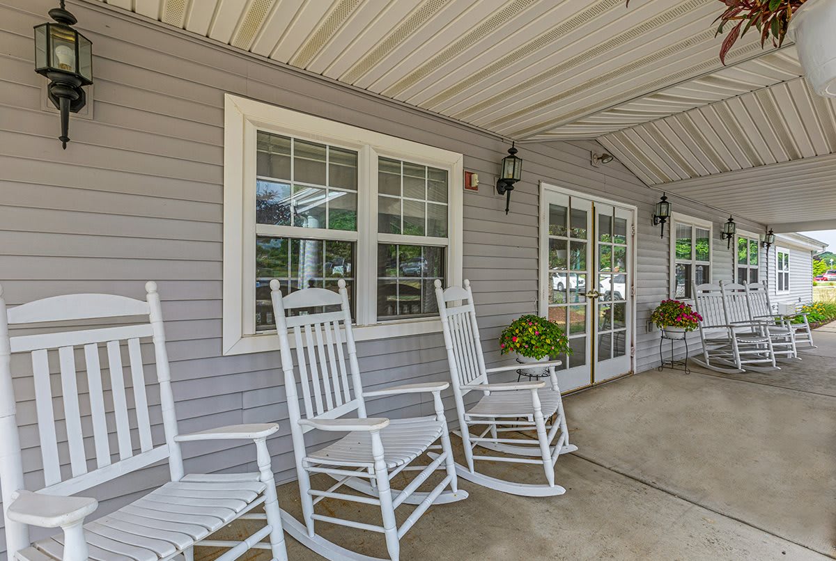 A cozy covered porch with white rocking chairs and potted plants.