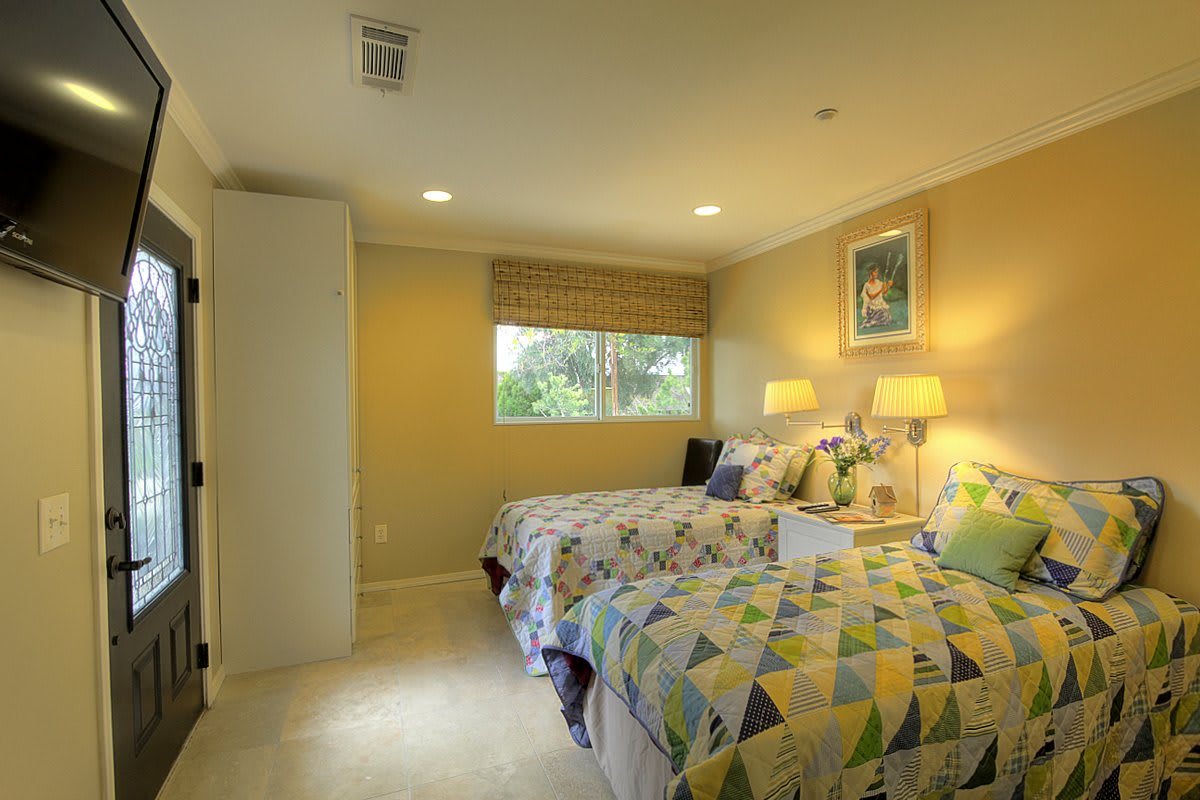 A cozy bedroom with twin beds, warm lighting, and a window view.