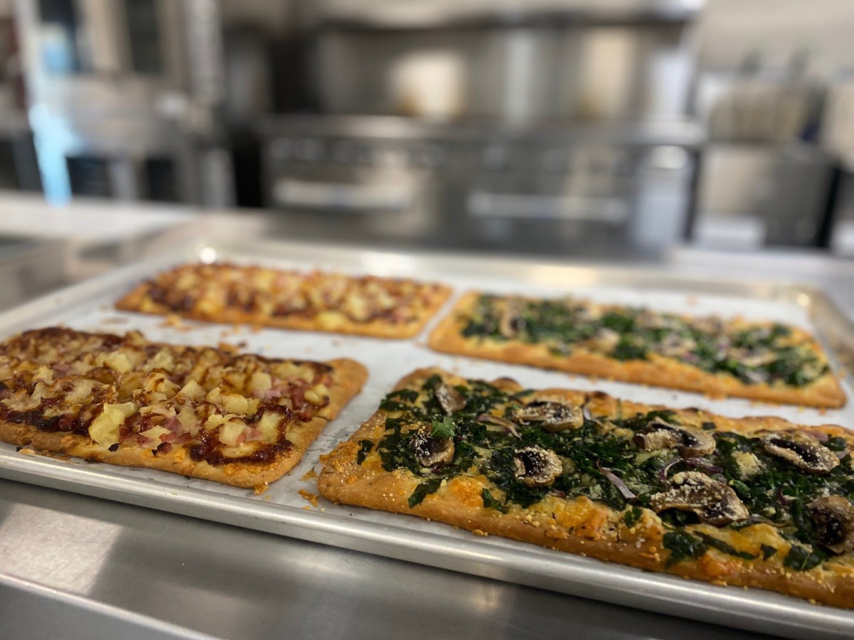 A tray of freshly baked flatbread pizzas with various toppings in a kitchen setting.