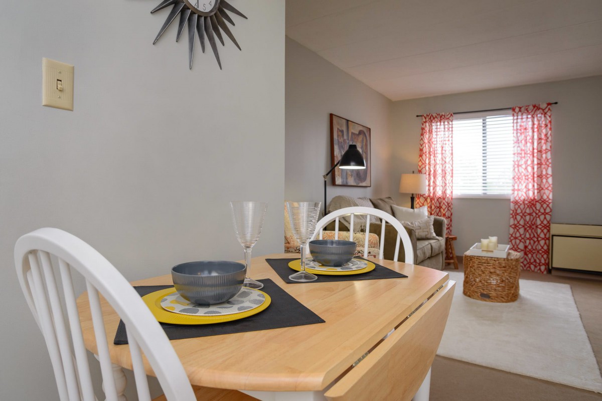 A cozy dining area with a neatly set table, leading into a bright living room.