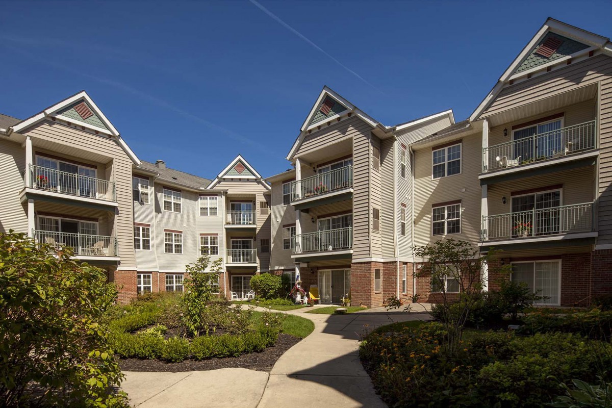 A modern apartment complex with well-maintained landscaping and balconies under a clear blue sky.