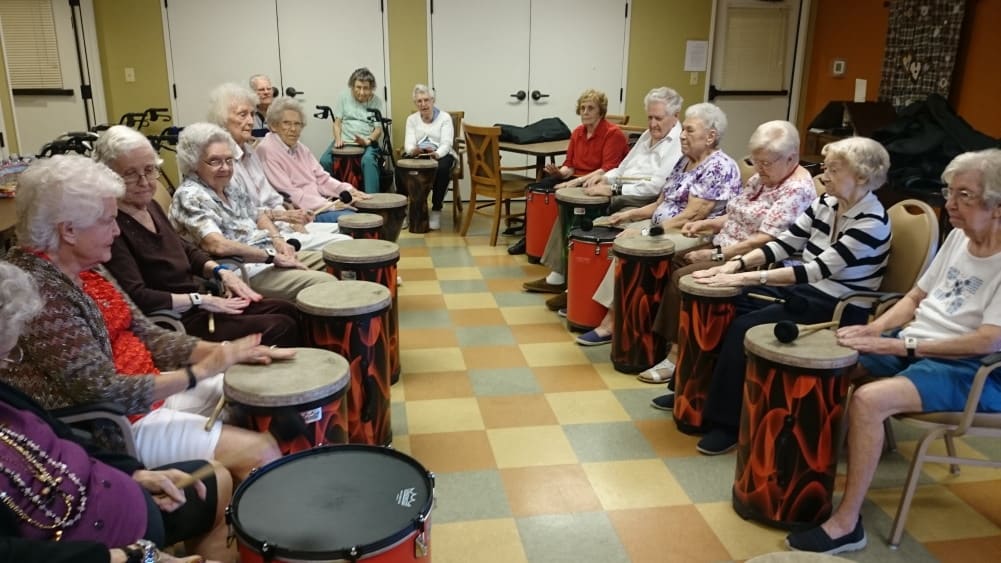 A group of seniors participating in a drumming circle activity indoors.