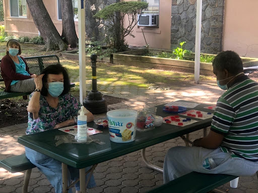 Two individuals enjoying a conversation at a park table, both wearing face masks.