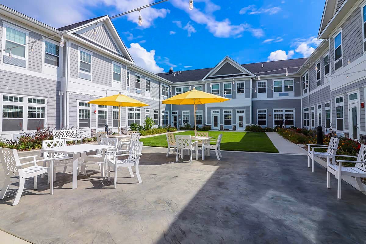 A sunny day at a residential building with outdoor seating and umbrellas in the courtyard.