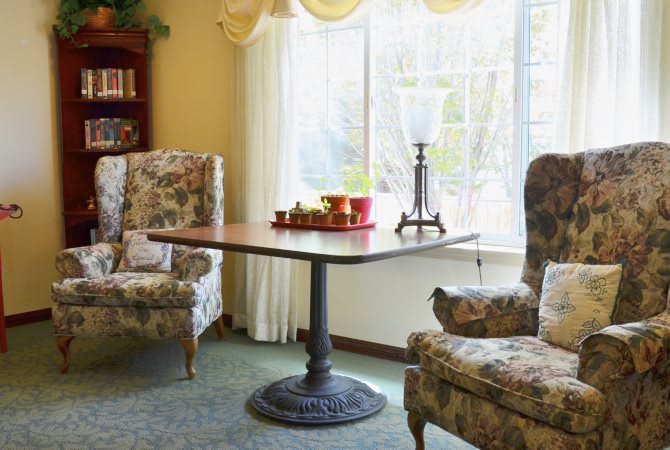A cozy living room with floral upholstered chairs and a table by the window.