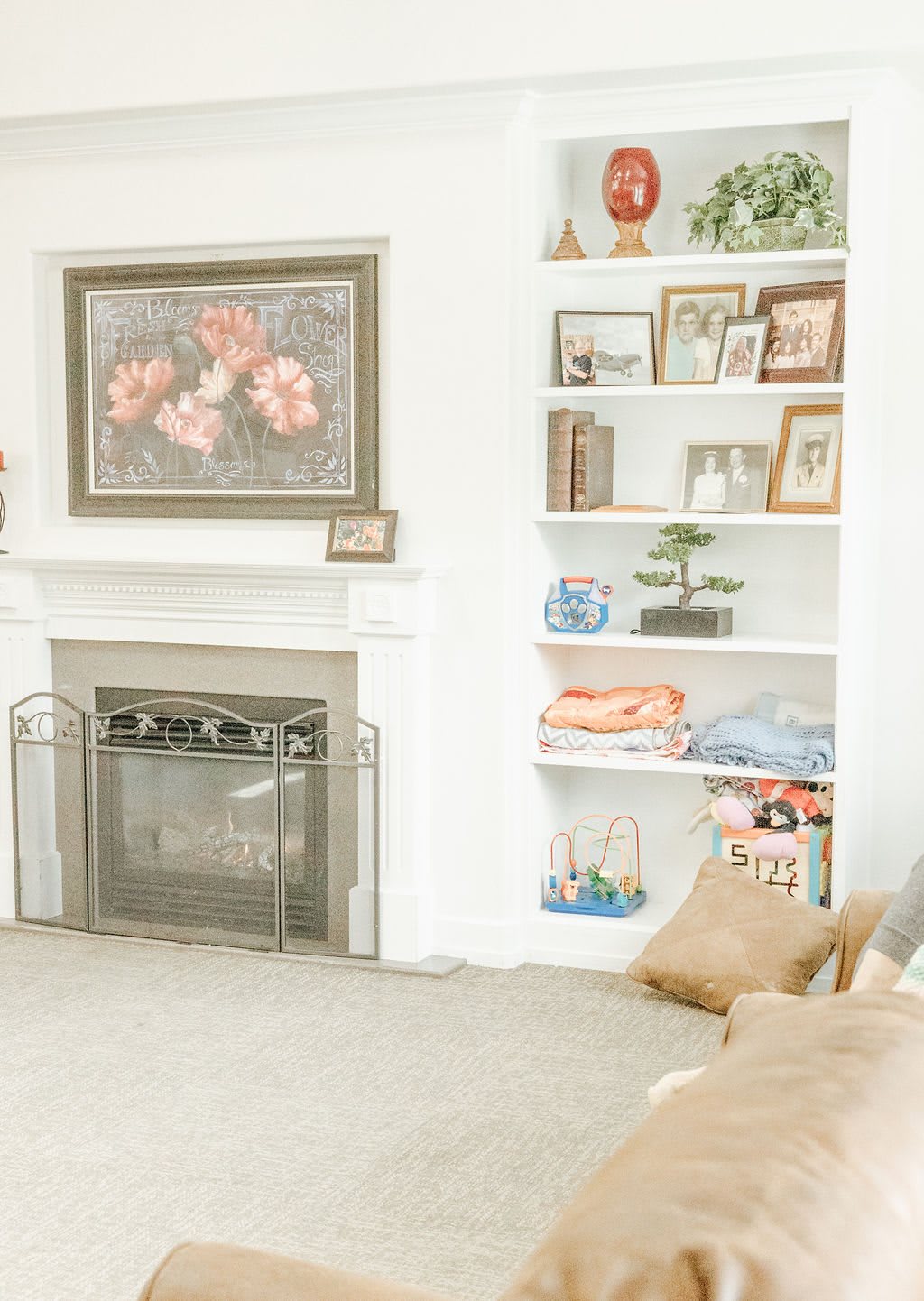 A cozy living room featuring a fireplace, decorated shelves, and framed artwork.