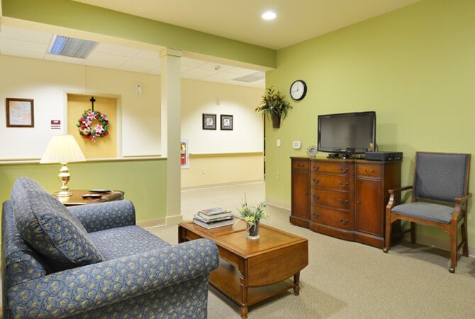 A cozy living room with green walls, featuring a sofa, wooden table, and television.
