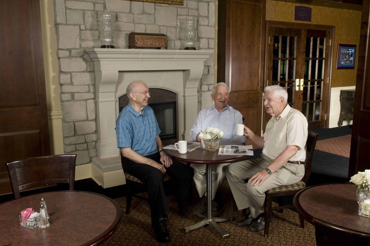 Three elderly men enjoying a conversation around a table with coffee in a cozy indoor setting.
