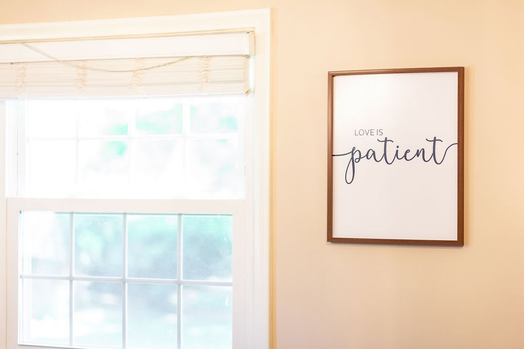 A cozy room with a window and wall art displaying the phrase 'Love is patient.'