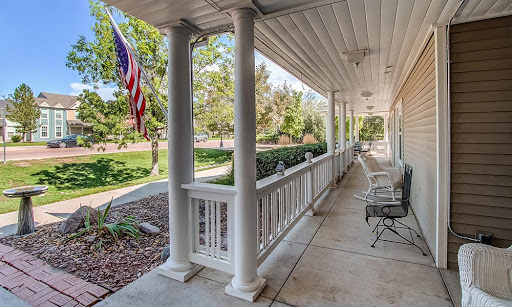 A serene porch view featuring classic columns, outdoor seating, and a waving American flag against a backdrop of lush greenery.