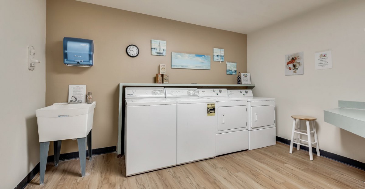 A modern laundry room featuring multiple washing machines and a dryer, with decorative wall art and a tidy appearance.