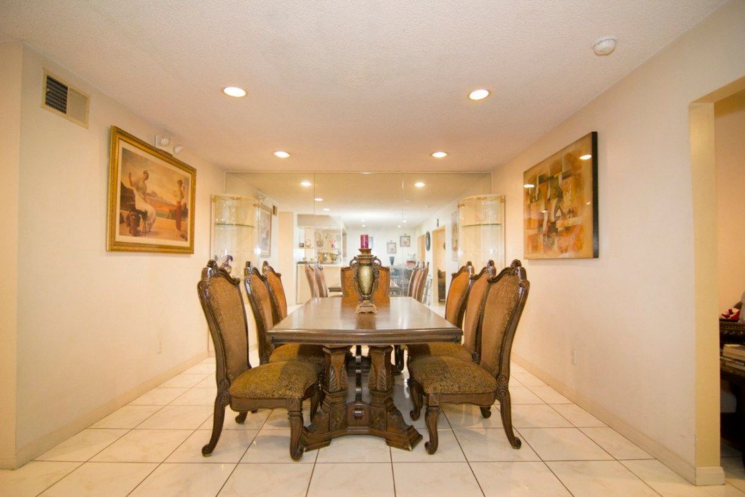 Elegant dining room with a large wooden table and ornate chairs, surrounded by artwork and soft lighting.