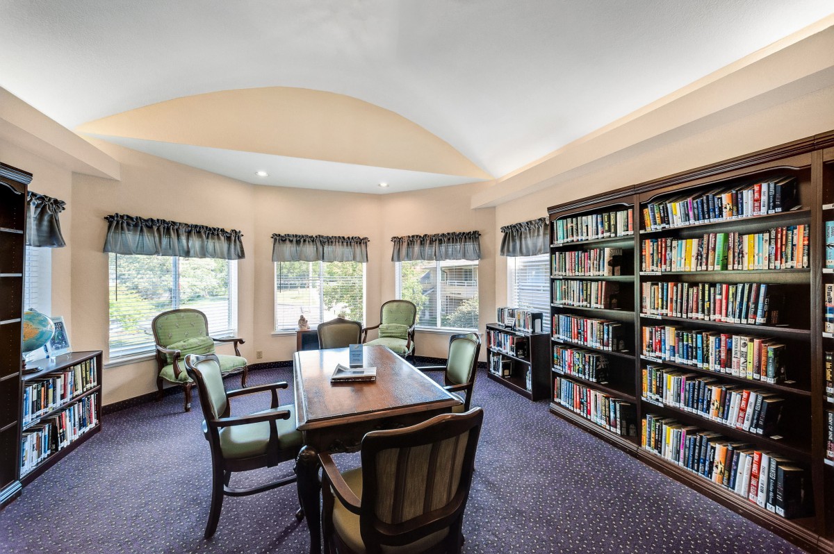 A cozy library room with bookshelves, a central table, and several chairs.