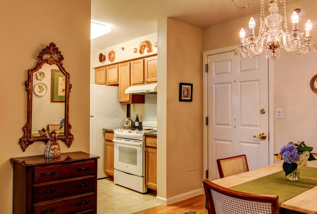 A cozy kitchen and dining area with wooden cabinets, a white stove, a chandelier, and a decorative mirror.
