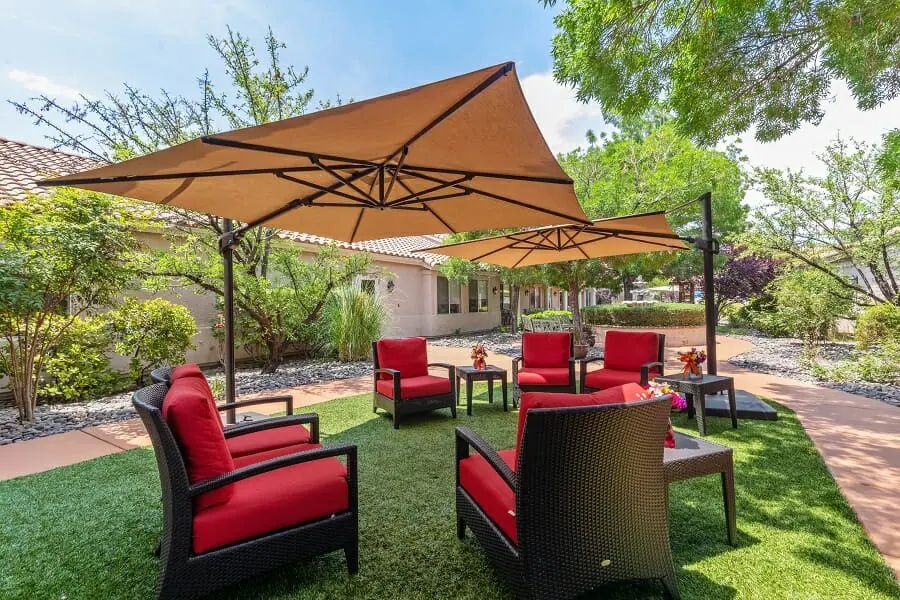 A cozy outdoor patio setup with red cushioned chairs and large umbrellas in a garden setting.