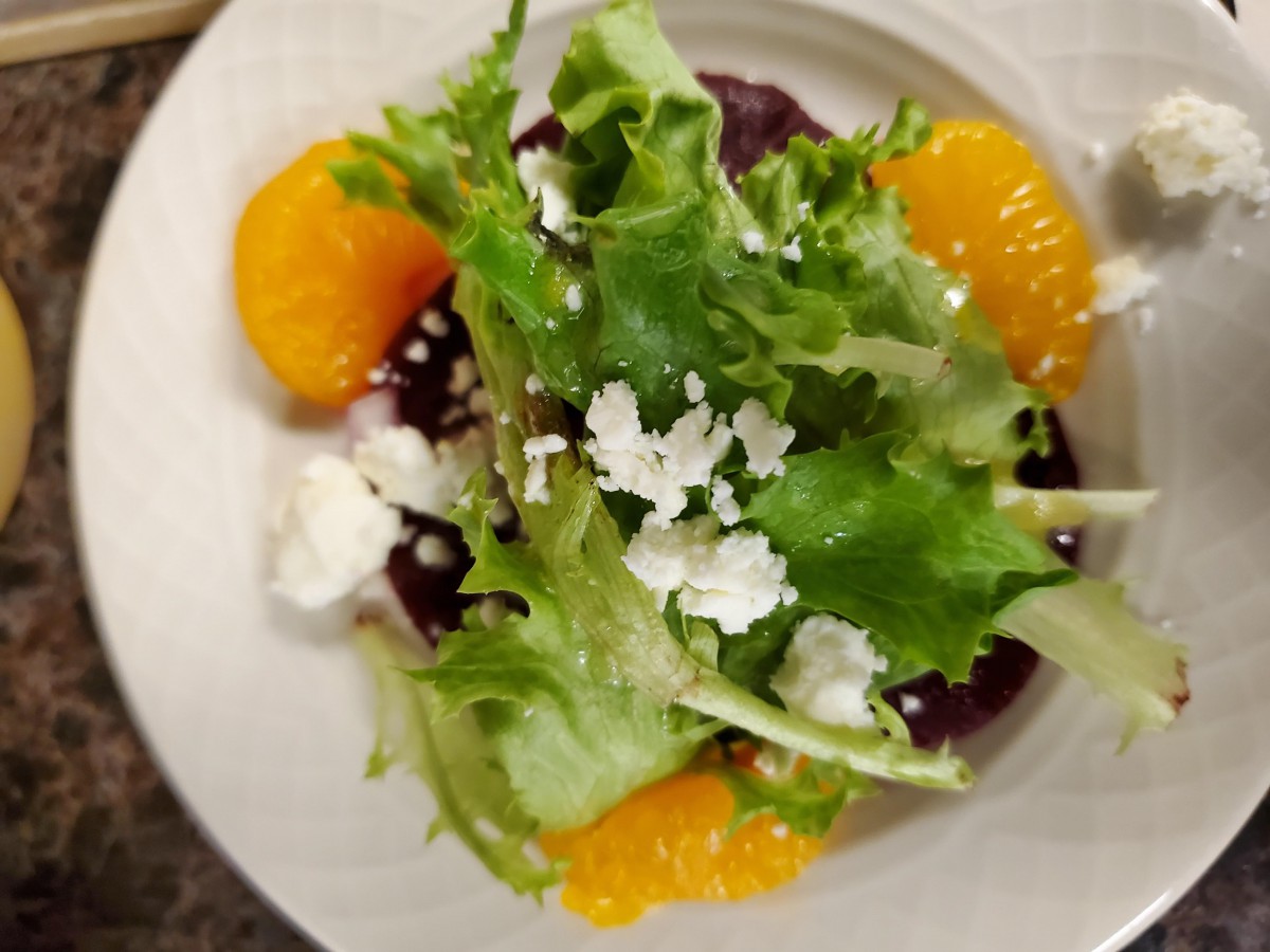A fresh salad featuring greens, orange slices, and crumbled cheese on a plate.