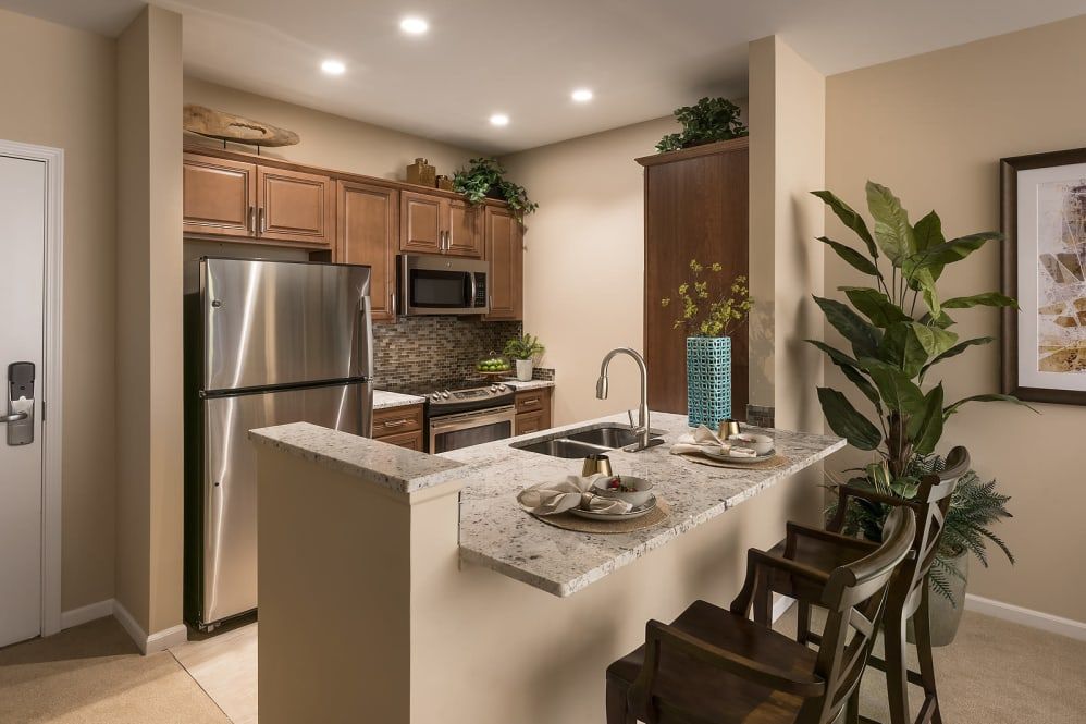 A modern kitchen featuring stainless steel appliances, wooden cabinets, and a cozy seating area with bar stools.