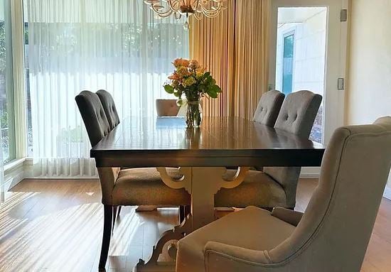 A beautifully set dining room with an elegant table adorned with a flower centerpiece and surrounded by upholstered chairs beneath a sparkling chandelier.