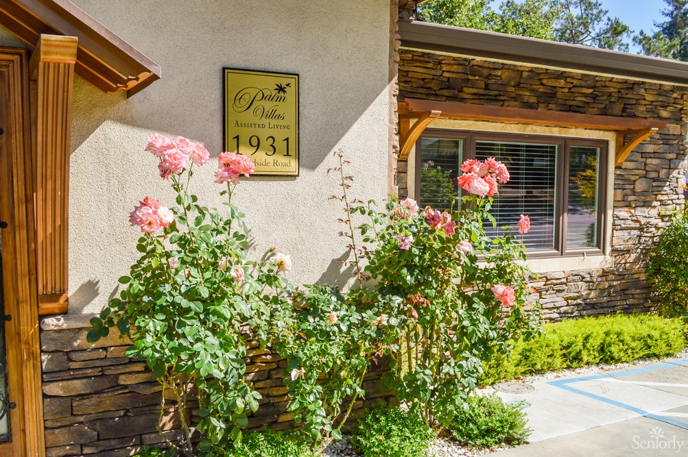 A charming building exterior with blooming roses in a sunny garden, featuring a plaque on the wall.