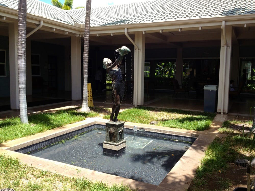 A statue stands in the center of a small fountain located in an outdoor courtyard.