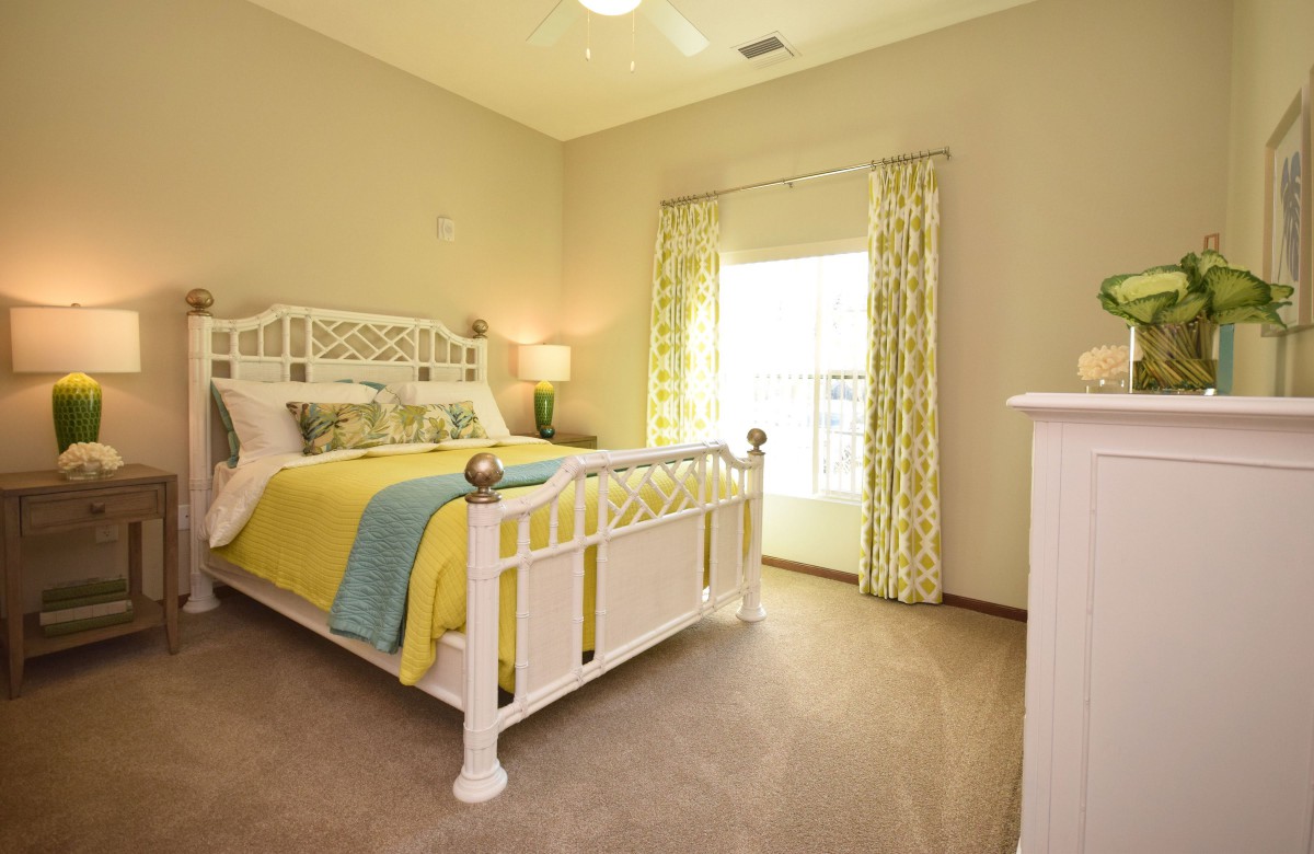 A bright and cozy bedroom with a white bed, colorful bedding, and large window curtains.