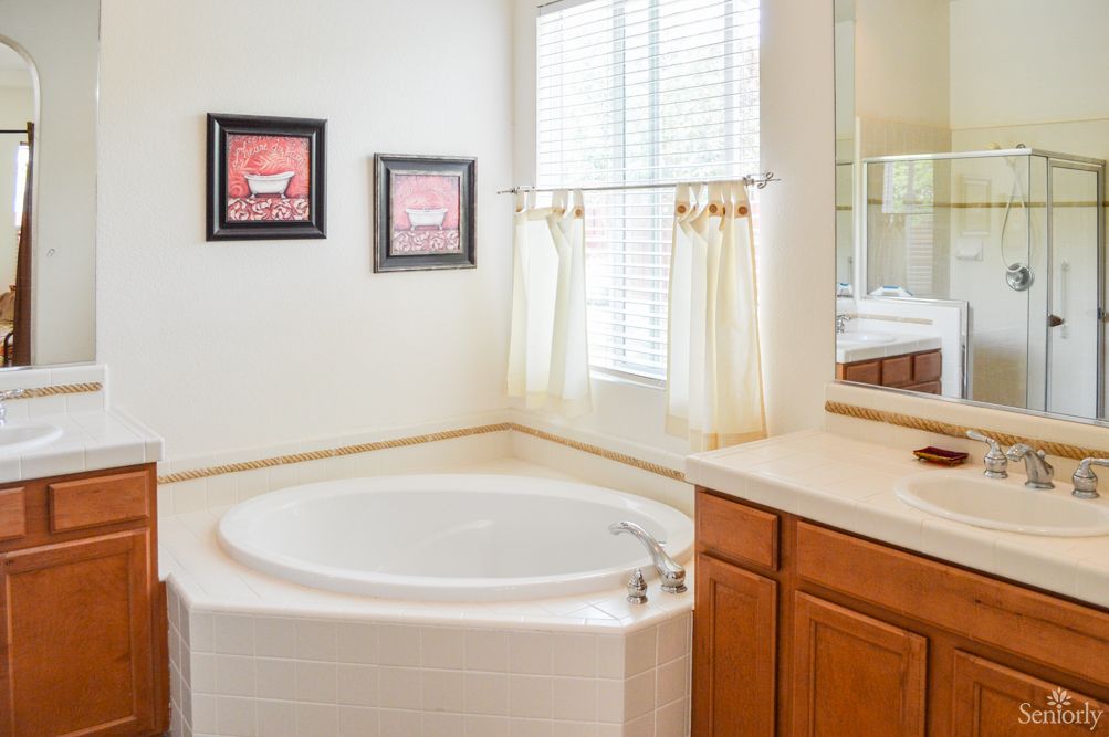 A bright bathroom with a circular bathtub, wooden cabinets, and artwork on the walls.