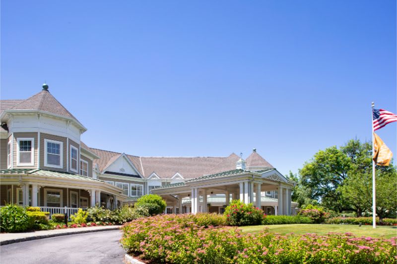 A large, elegant house surrounded by a well-maintained garden under a clear blue sky.