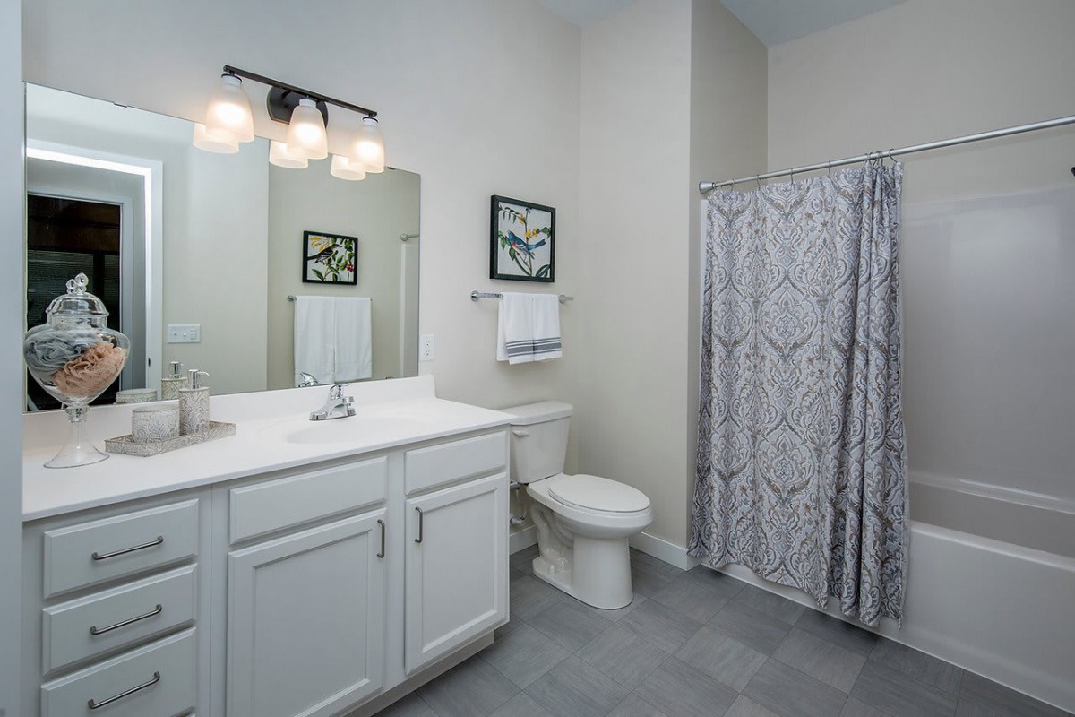 A clean and modern bathroom with a white vanity, mirror, toilet, and patterned shower curtain.
