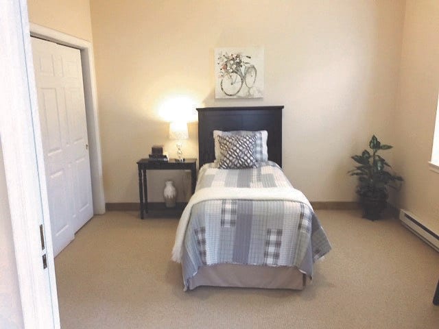 A cozy bedroom with a single bed, nightstand, lamp, and decorative elements.
